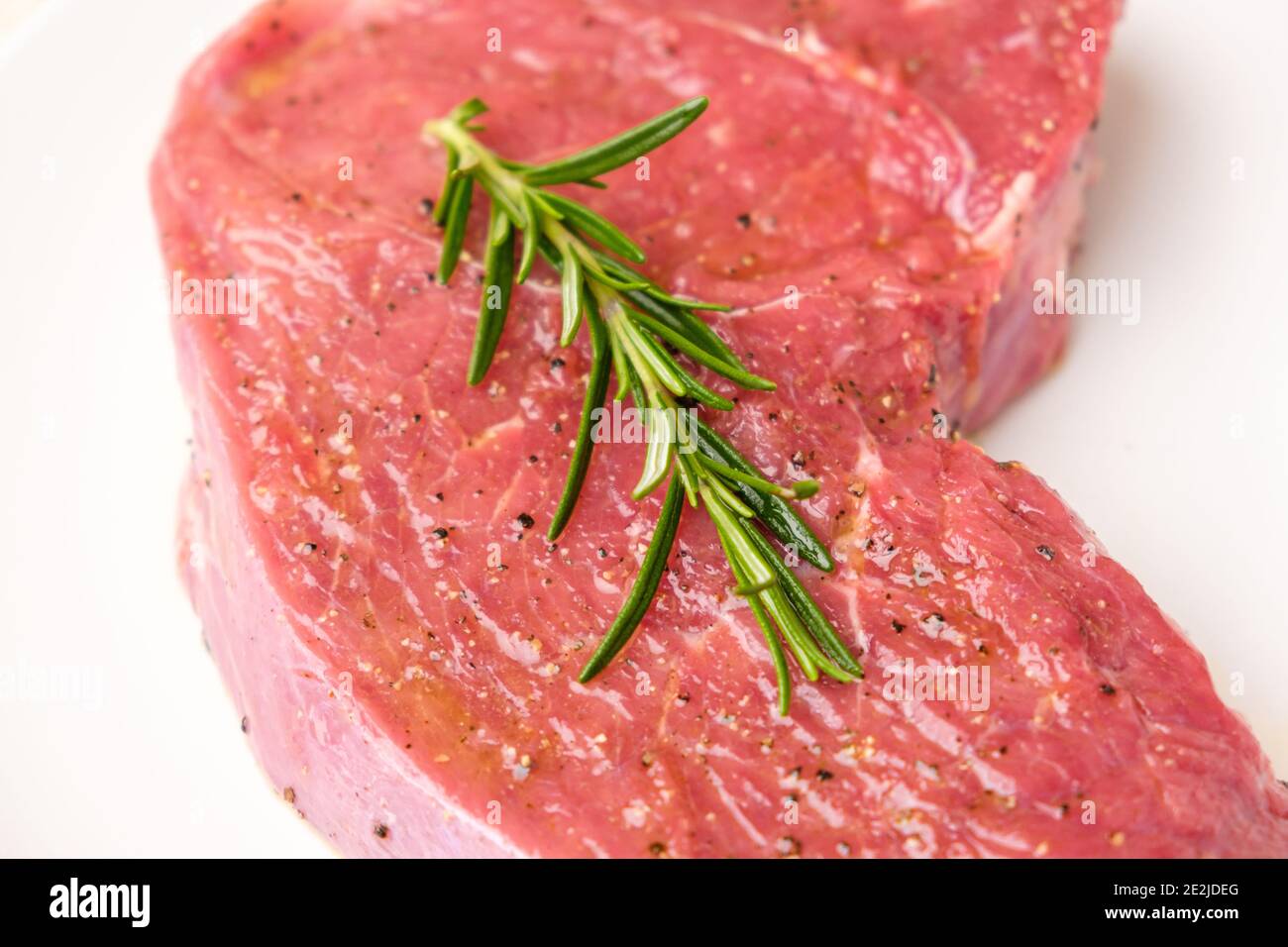 Rohes Rindersteak Fleisch mit Zweig von Rosmarin und Arten isoliert auf ... Rohes Rindersteak Fleisch mit Zweig von Rosmarin und Arten isoliert auf ...