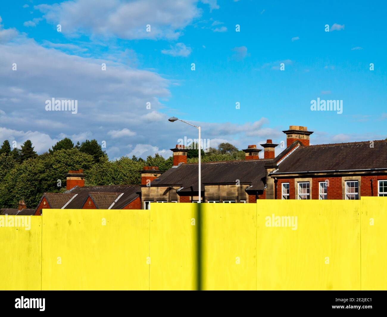Heller hölzerner Sicherheitszaun mit Gebäuden im Hintergrund und blauem Himmel darüber. Stockfoto
