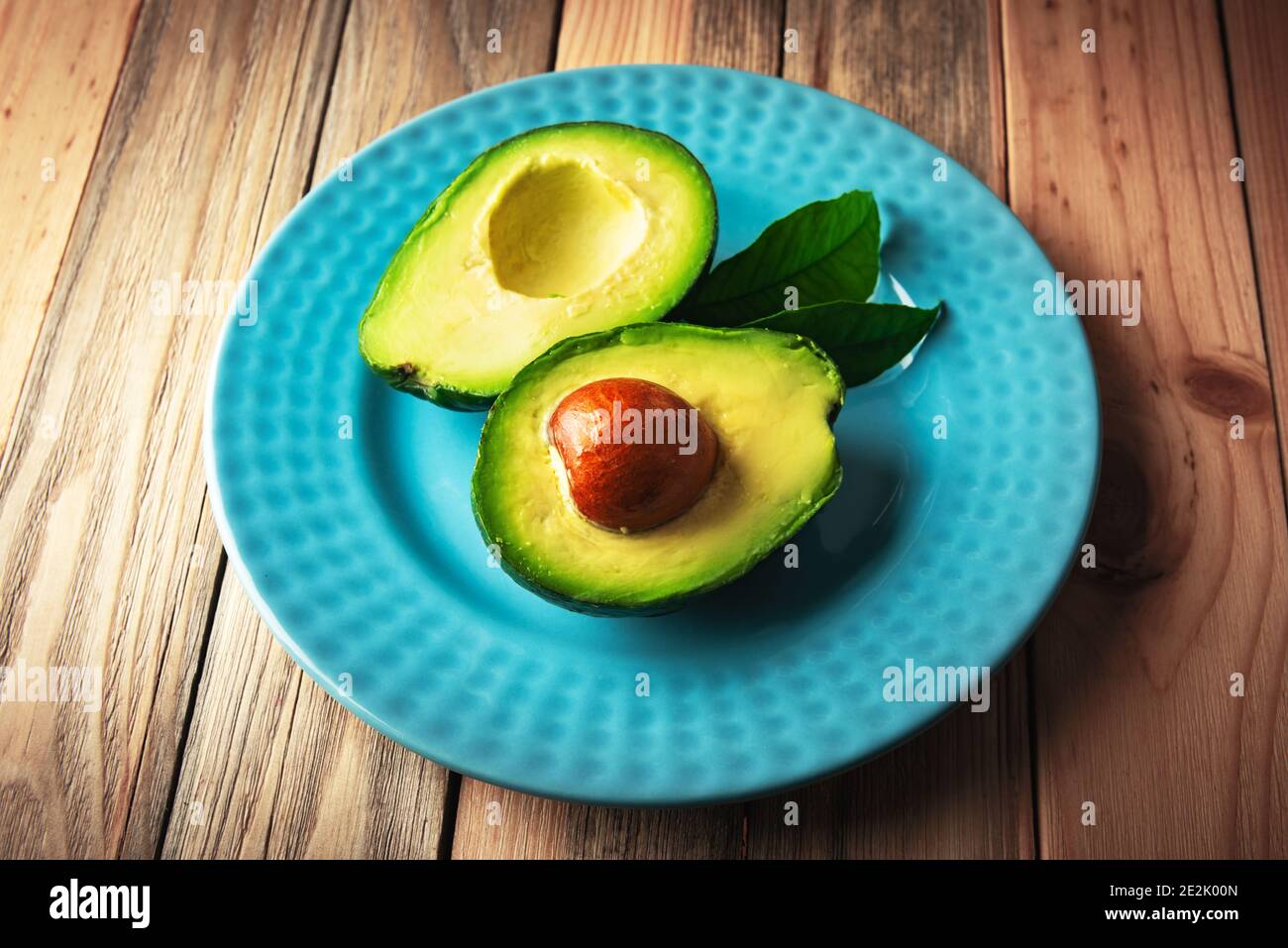 Frische Avocado-Früchte auf einem blauen Teller auf einem Holztisch. Das Konzept der gesunden Ernährung. Food-Fotografie Stockfoto