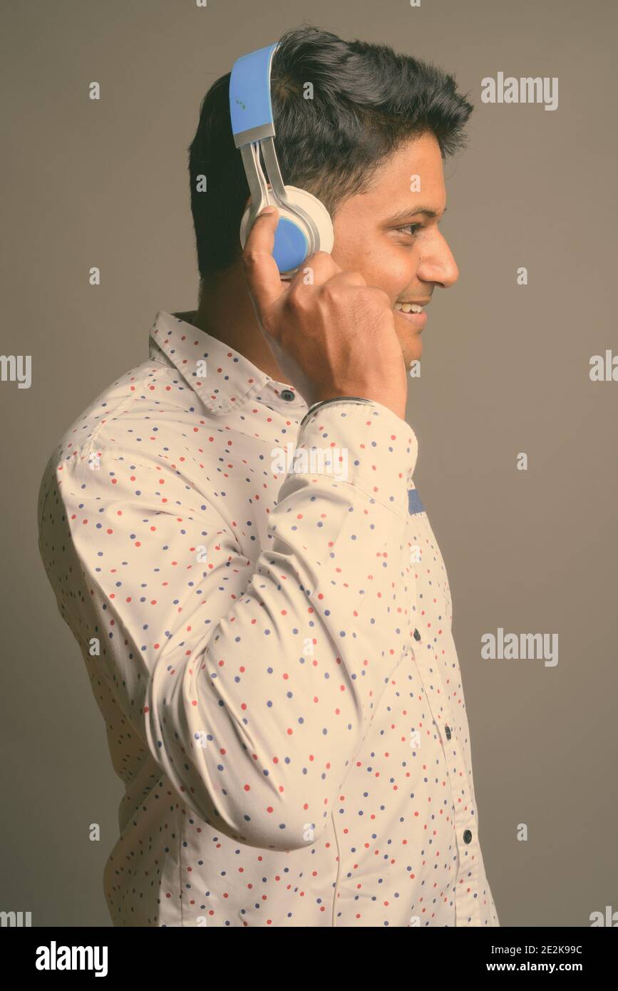 Junger indischer Geschäftsmann, der vor grauem Hintergrund Musik hört Stockfoto