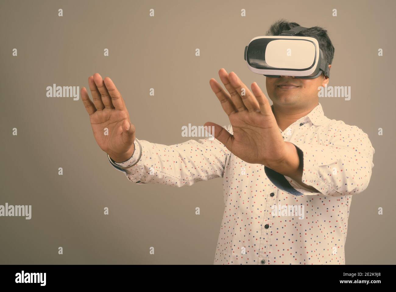 Junge indische Geschäftsmann mit Virtual Reality-Headset vor grauem Hintergrund Stockfoto
