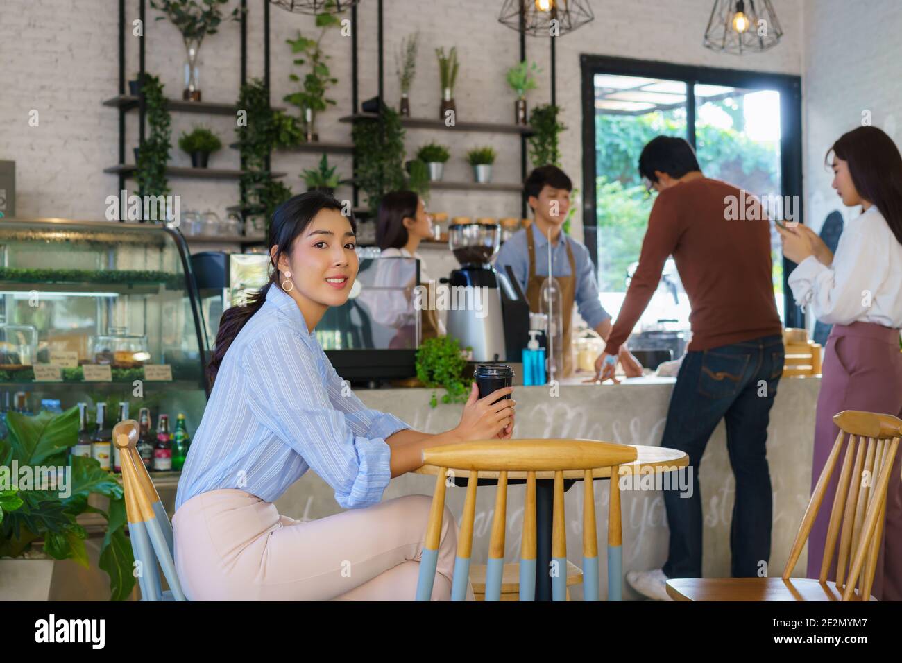 Asiatische Frau sitzt im Café und glücklich fühlen, während sie Kaffee trinken und andere Leute Schlange Getränke mit Barista bestellen. Stockfoto