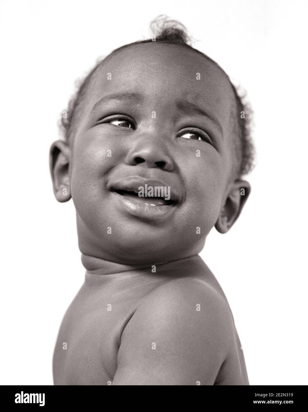 1940ER LÄCHELNDER AFROAMERIKANISCHER BABY JUNGE, DER AUF UND ZURÜCK SCHAUT ÜBER SEINER SCHULTER - N266 HAR001 HARS UND SCHWARZE ETHNIE BIS BABY JUNGE JUGENDLICHE SUCHEN SCHWARZ UND WEISS HAR001 ALTMODISCHE AFROAMERIKANER Stockfoto