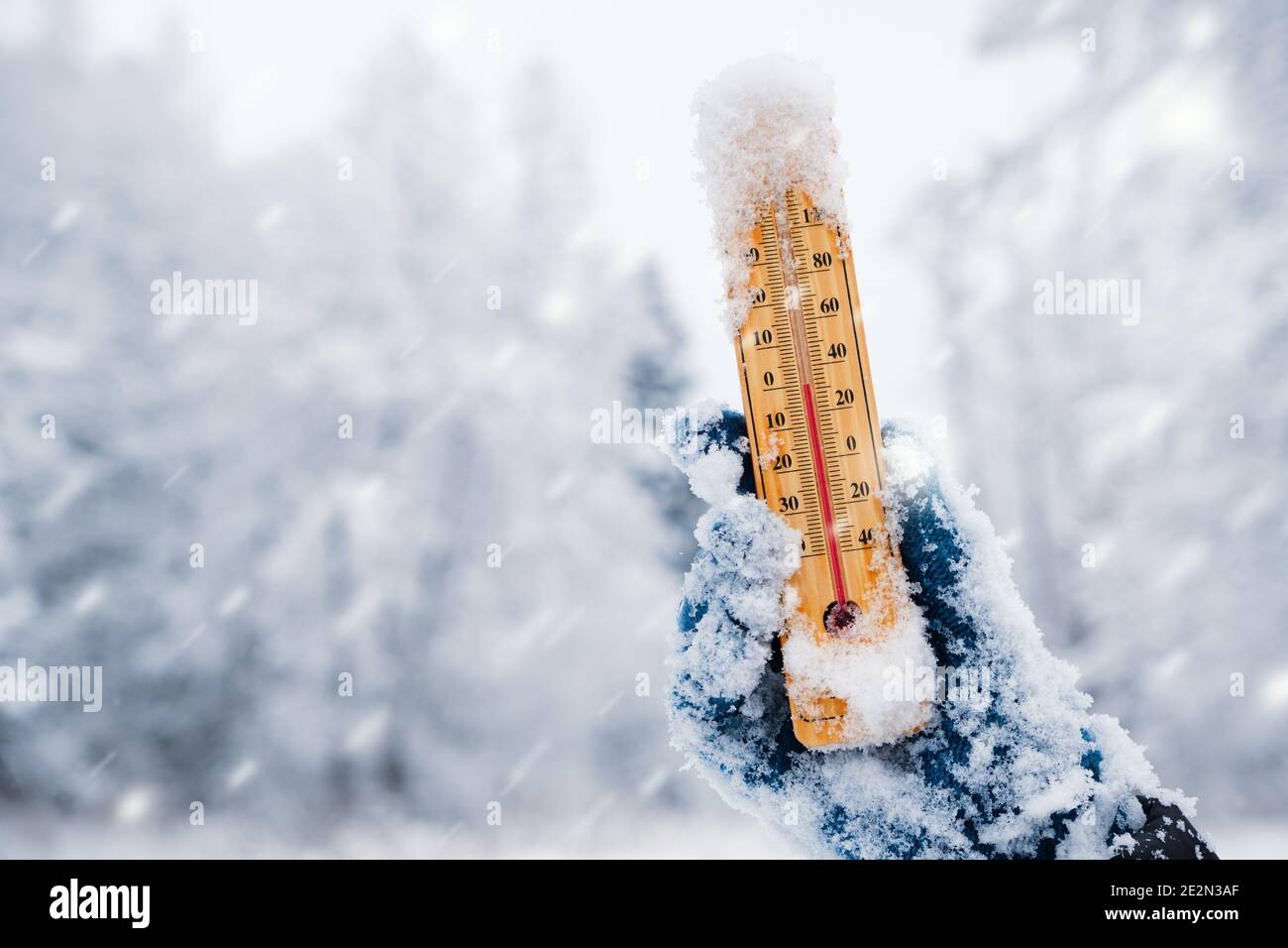 Menschliche Hand hält ein Thermometer mit der niedrigen Temperatur gegen Winter Natur Hintergrund mit Schneefall. Stockfoto