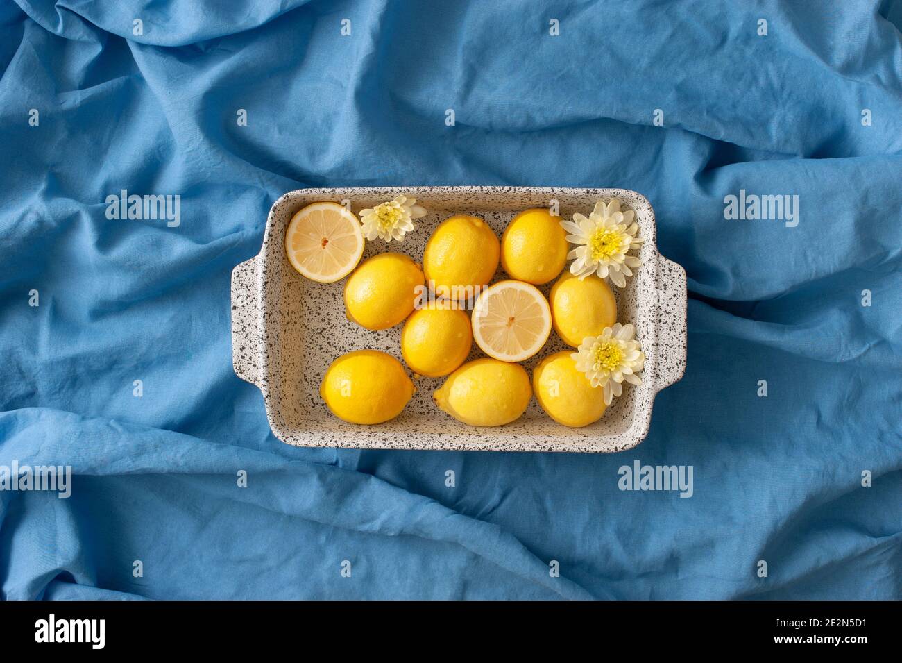 Sommerarrangement mit Zitronen und gelben Blumen in einem Wasserbad auf einem blauen Leinentuch. Abstrakter Hintergrund. Stockfoto