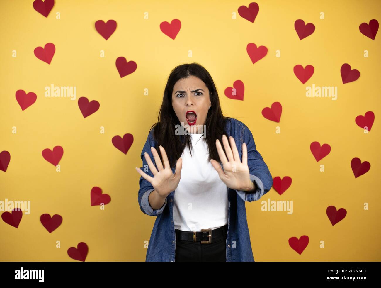 Junge kaukasische Frau auf gelbem Hintergrund mit roten Herzen Angst und erschrocken vor Angst Ausdruck Stop Geste mit Händen, schreien im Schock. Schwenken Stockfoto