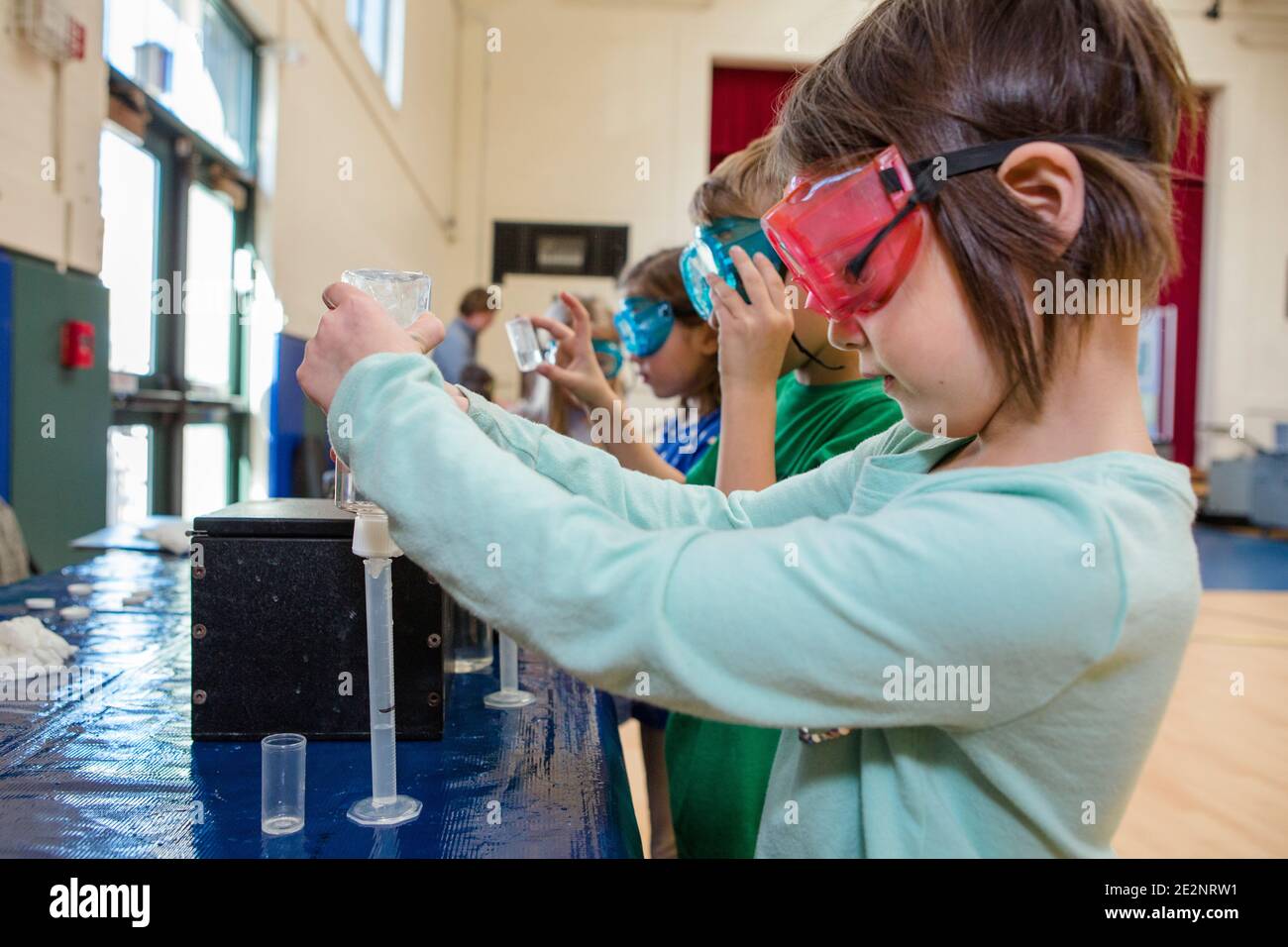 Ein kleines Mädchen in Schutzbrille misst Flüssigkeit in ein Reagenzglas Stockfoto