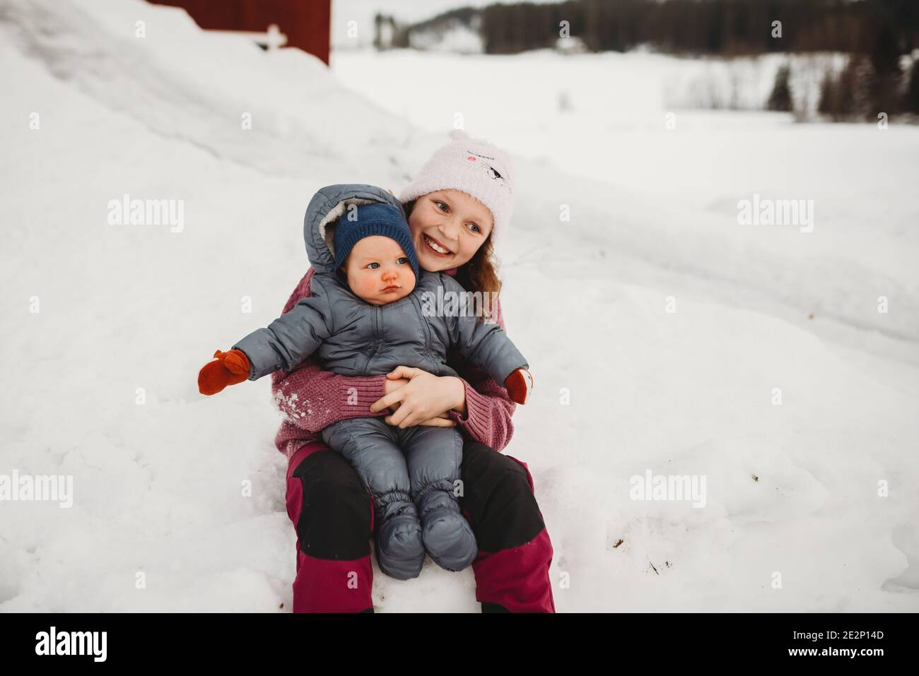 Smiley große Schwester hält Baby Bruder draußen im Schnee Bei kaltem da Stockfoto