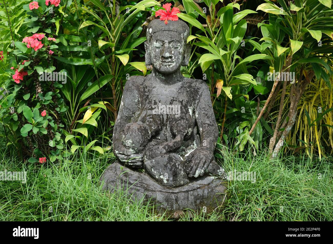 Indonesien Bali - Ubud Handgefertigte Buddha Statue aus Stein mit rot Hibiskusblüte Stockfoto