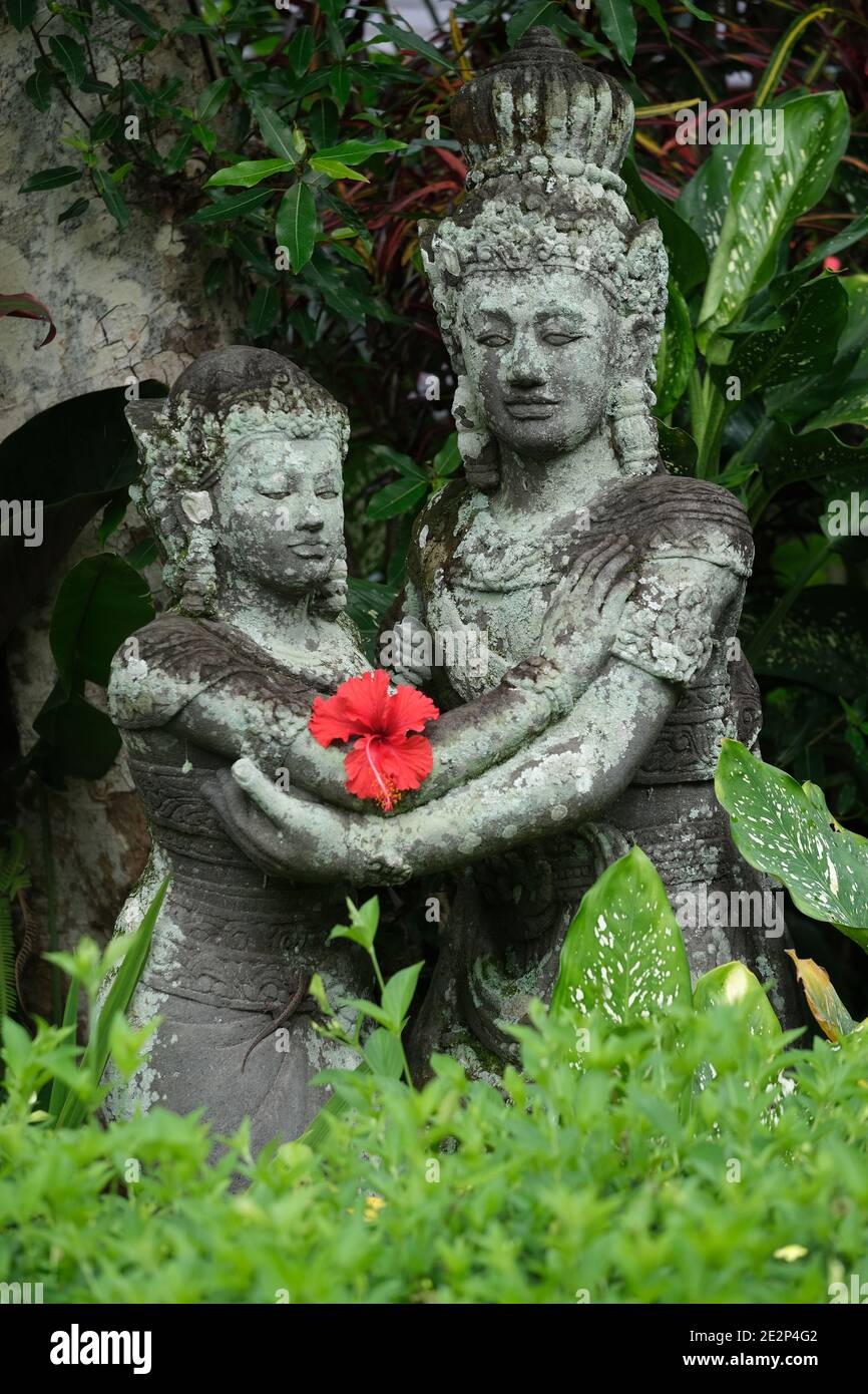 Indonesien Bali - Ubud Handgefertigte Steinstatuen mit rotem Hibiskus Blume vertikal Stockfoto