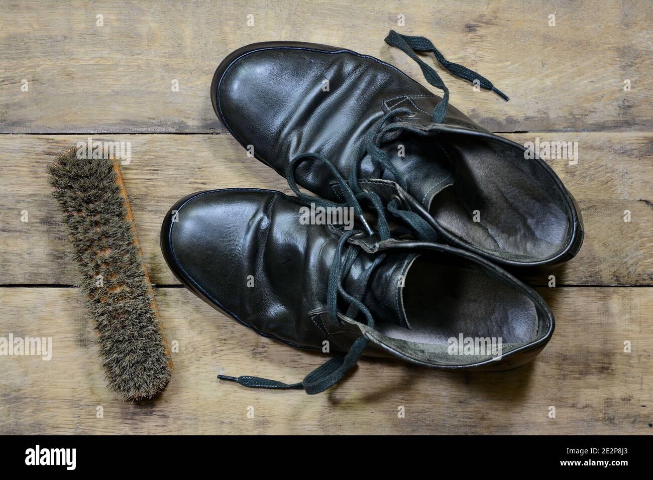 Alte Lederschuhe mit Schuhpolitur und Bürsten gegen Alter Gesprungene Holzbretter Stockfoto