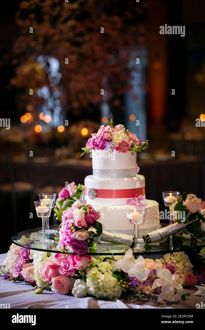 Weiße Frosting Hochzeitstorte mit rosa Bändern und Blumen verziert Für eine abendliche Hochzeitszeremonie Stockfoto