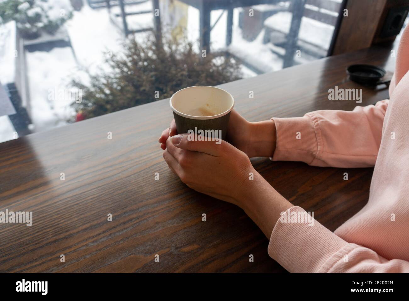 Ein Mädchen in einem rosa Pullover hält einen Papierbecher Mit zwei Händen mit Kaffee an einem Wintertag Stockfoto