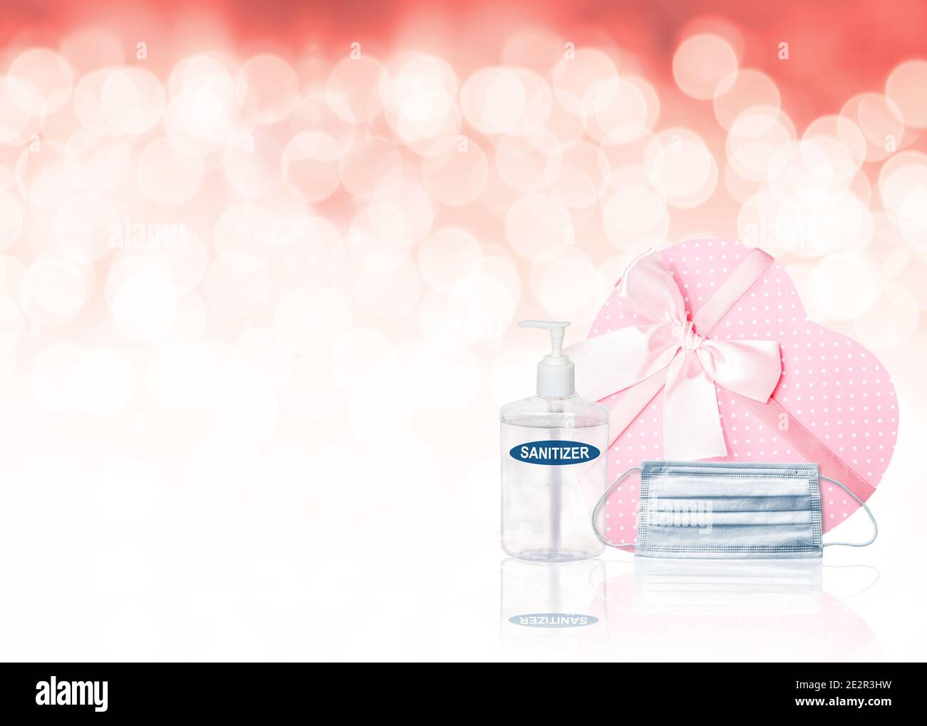 Valentinstag Konzept während Covid-19 Pandemie mit herzförmigen rosa Geschenkbox, Gesichtsmaske, Hand-Desinfektionsmittel und Kopierer Platz auf rosa Bokeh Hintergrund. R Stockfoto