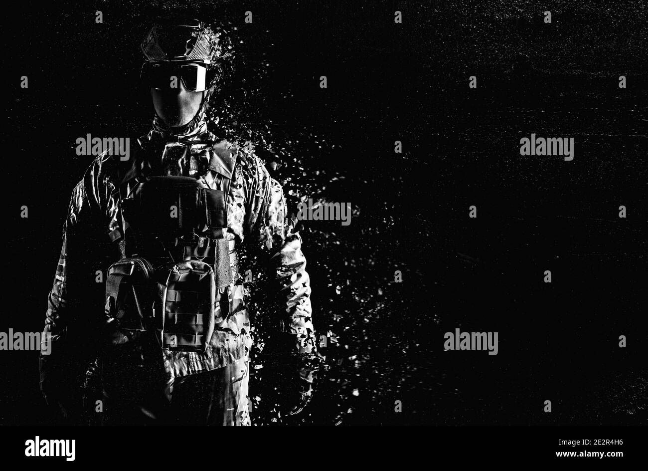 Schwarz-Weiß-Foto eines voll ausgerüsteten Soldaten, der in taktischer Kleidung steht und sich auf grungigem schwarzem Hintergrund auflöst. Stockfoto