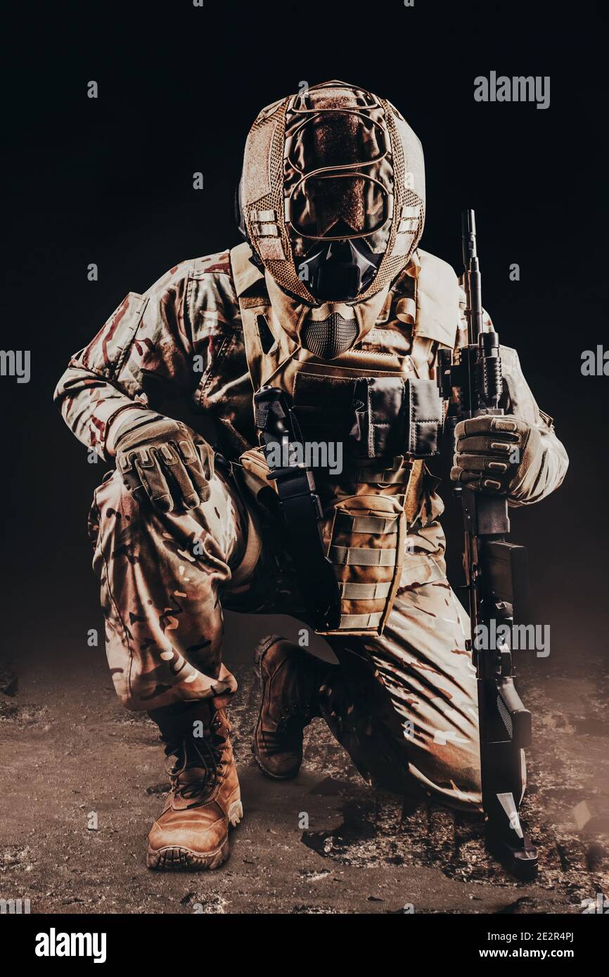 Foto eines voll ausgerüsteten Soldaten in gepanzerter Weste. Helm und getarntes Outfit kniend mit Gewehr auf schwarzem Hintergrund. Stockfoto