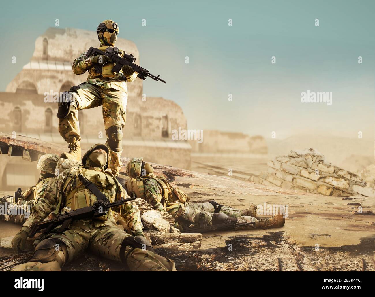 Foto eines voll ausgerüsteten Soldaten in gepanzerter Weste, Helm und Gewehr stehen auf einem Felsen mit gefallenen Soldaten unter ihm in der Wüste zerstörte Stadt. Stockfoto