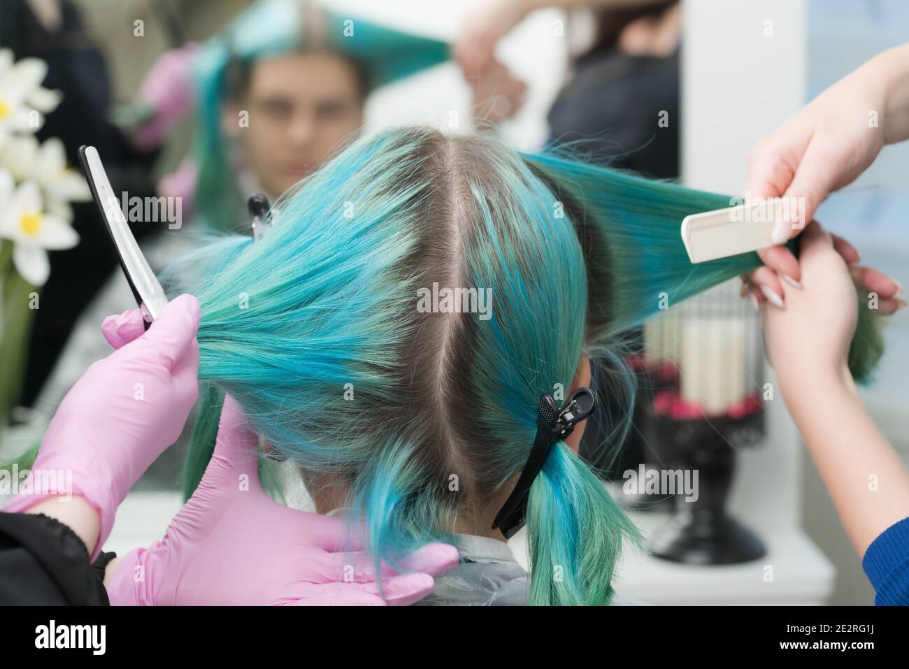 Zwei Friseure Kämmen Kunden Haare vor dem Haarfärbeprozess. Rückansicht des Frauenkopfes mit smaragdgrüner Haarfarbe und nachwachsende Haarwurzeln Stockfoto
