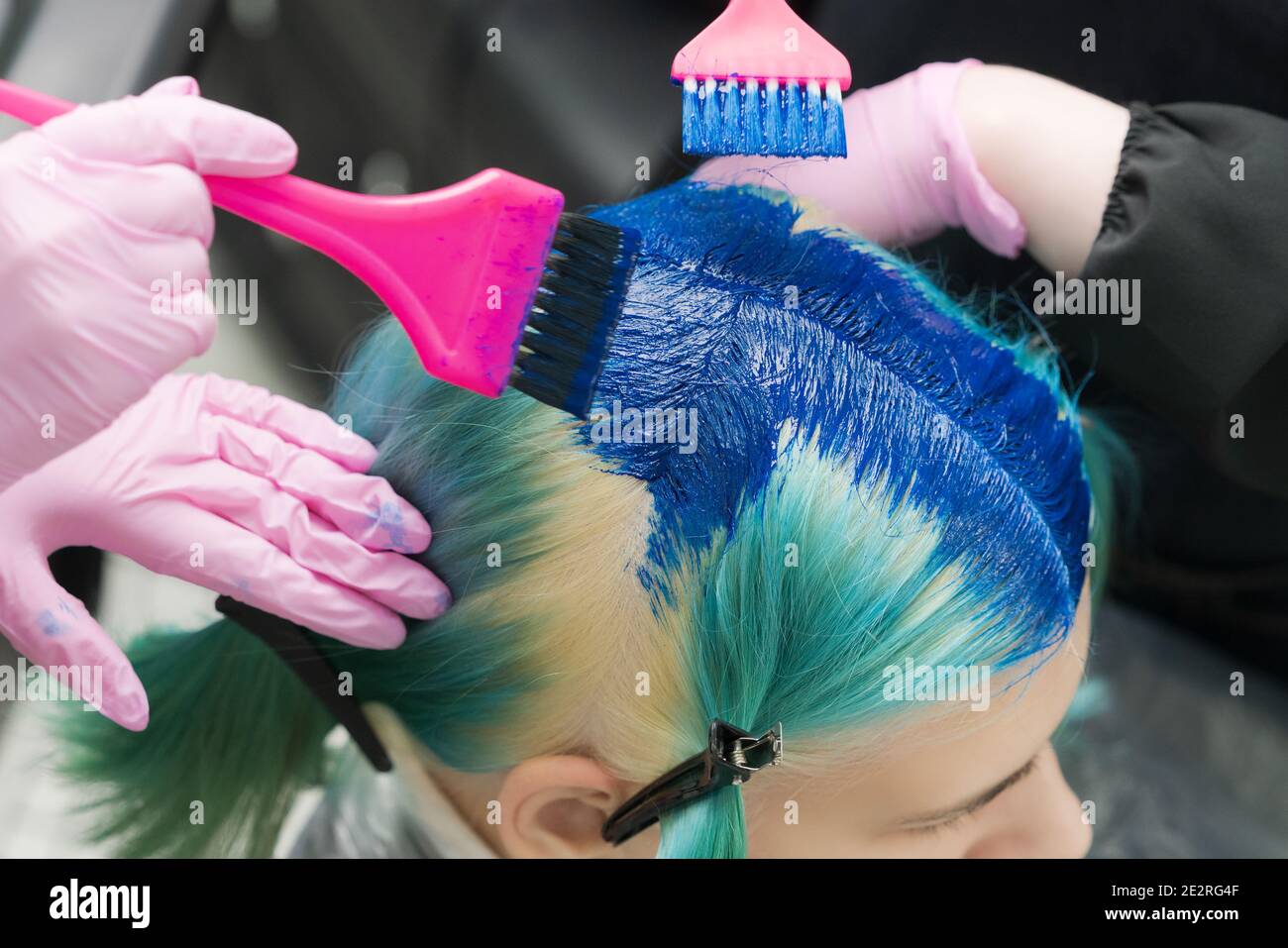Zwei Friseure mit rosa Pinsel beim Auftragen von blauer Farbe auf weibliche Client mit smaragdgrünen Haarfarbe, während des Prozesses der Färbung Haar im Schönheitssalon Stockfoto