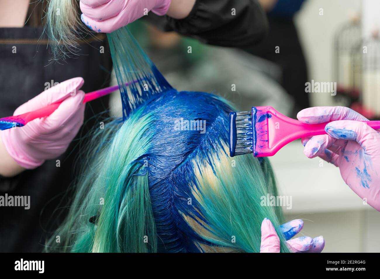 Zwei professionelle Friseure in Schutzhandschuh mit rosa Pinsel beim Auftragen von blauer Farbe auf weibliche mit smaragdgrünen Haarfarbe, Prozess des Färbens Haar Stockfoto