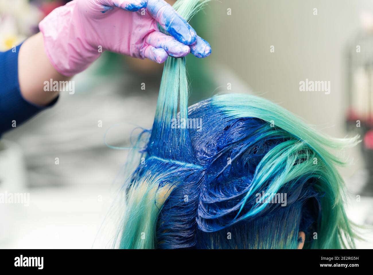 Friseure mit der Hand in schützenden Handschuh heben Schock der blauen Haare des Kunden während des Färbeprozesses im Schönheitssalon. Stockfoto