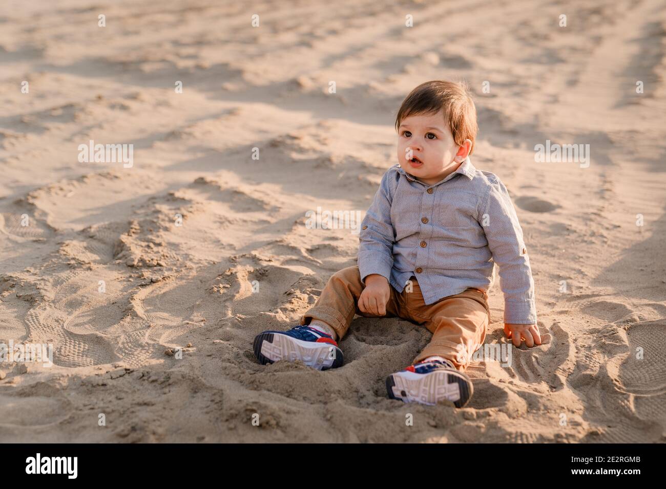 Einjähriger Junge sitzt im Sand, lächelt und spielt. Stockfoto