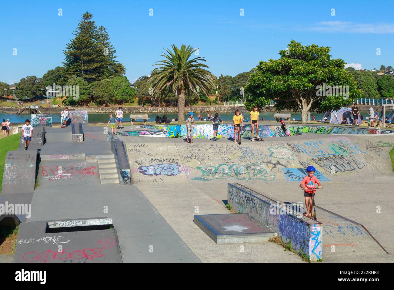 Kinder auf Rollern und Skateboards spielen in einem Skatepark. Raglan, Neuseeland Stockfoto
