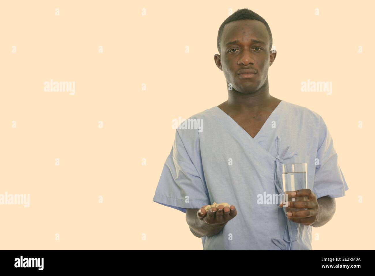 Studio shot von jungen schwarzen afrikanischen Mann patient Holding vitamin Tabletten und ein Glas Wasser Stockfoto