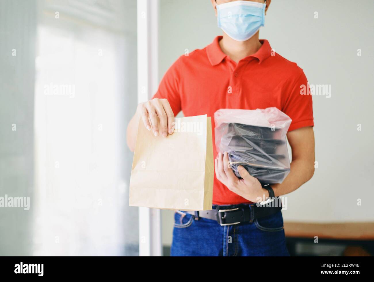 Lieferung Mann trägt schützende Gesichtsmaske Coronavirus und Hand halten Handwerk Papier Lebensmittelverpackung Service, Postmann und drücken verschiedene Papier contai Stockfoto