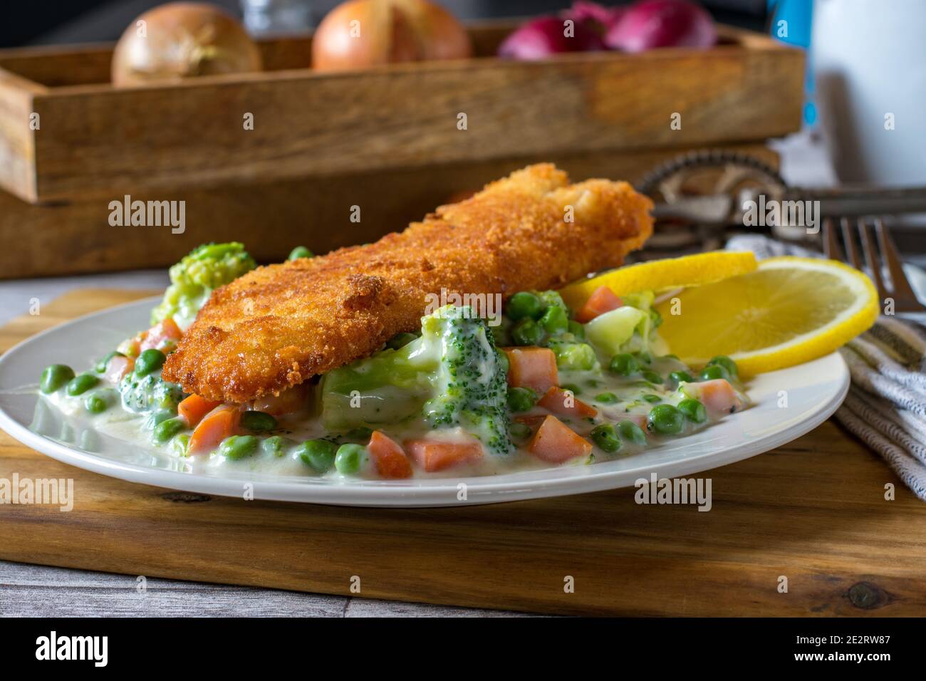 Panierter Fisch mit gemischtem Gemüse in cremiger Sauce Stockfoto