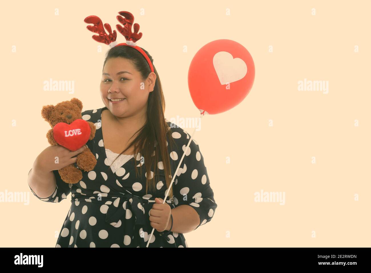Studio Schuss von jungen glücklich Fett asiatische Frau lächelnd während Halten Teddybär mit Herz und Liebe Zeichen während des Tragens Rentier Stirnband und halten rot Stockfoto