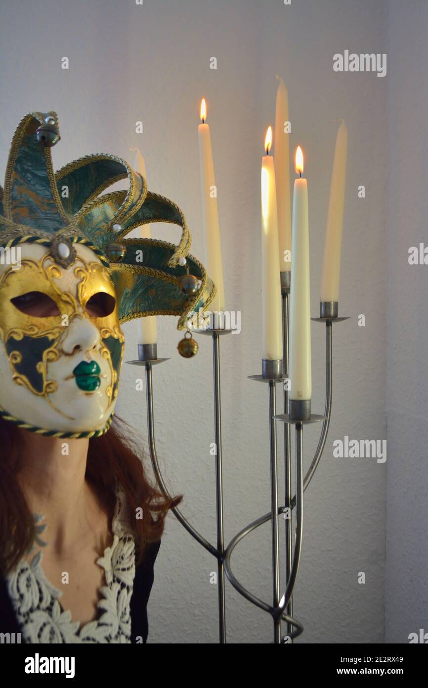 Kunstkonzept. Person verkleidet mit venezianischer Maske neben angezündeten Kerzen Stockfoto