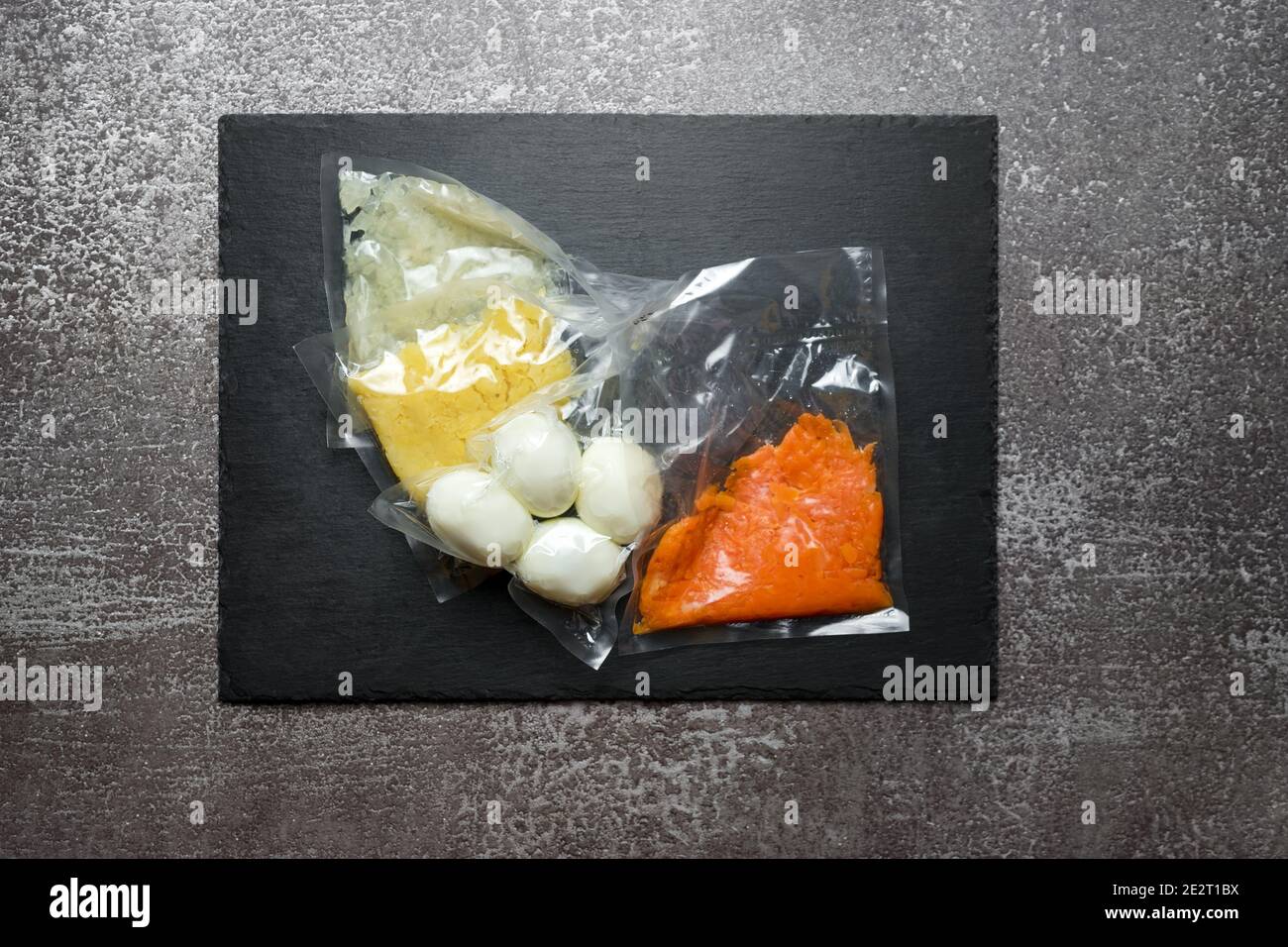 Produkte in Vakuumverpackung auf schwarzem Schiefertafel. Gekochte Eier und Gemüse für die Herstellung von Salat, vakuumversiegelte Lebensmittel bereit für Sous Vide Kochen. Sous-V Stockfoto
