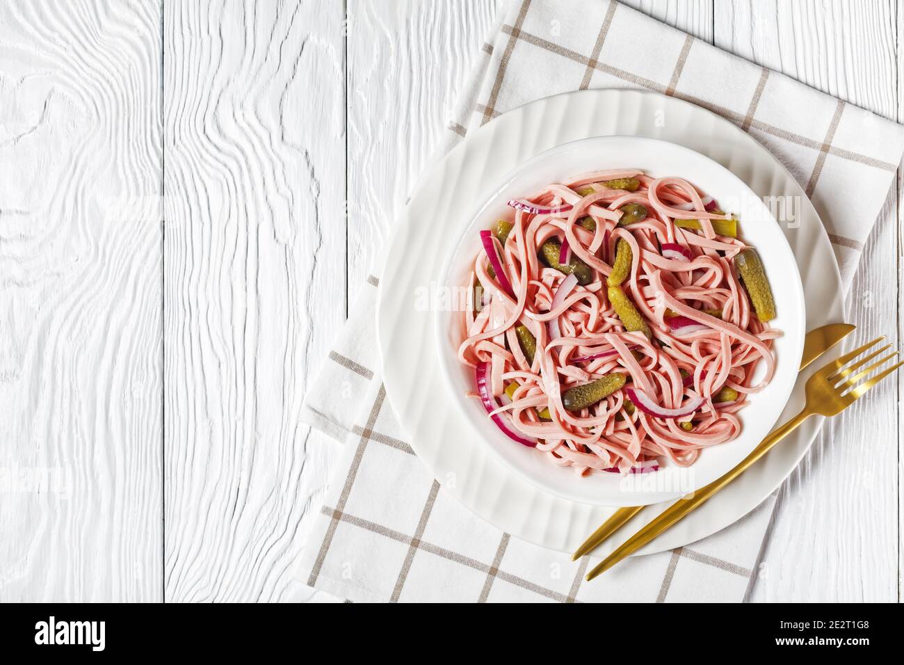 Deutscher Wurstsalat Wurstsalat aus geschnittener lyoner-Wurst mit Gurken Und rote Zwiebel serviert auf einem weißen Teller mit goldenen Besteck und Serviette auf einem weißen Stockfoto