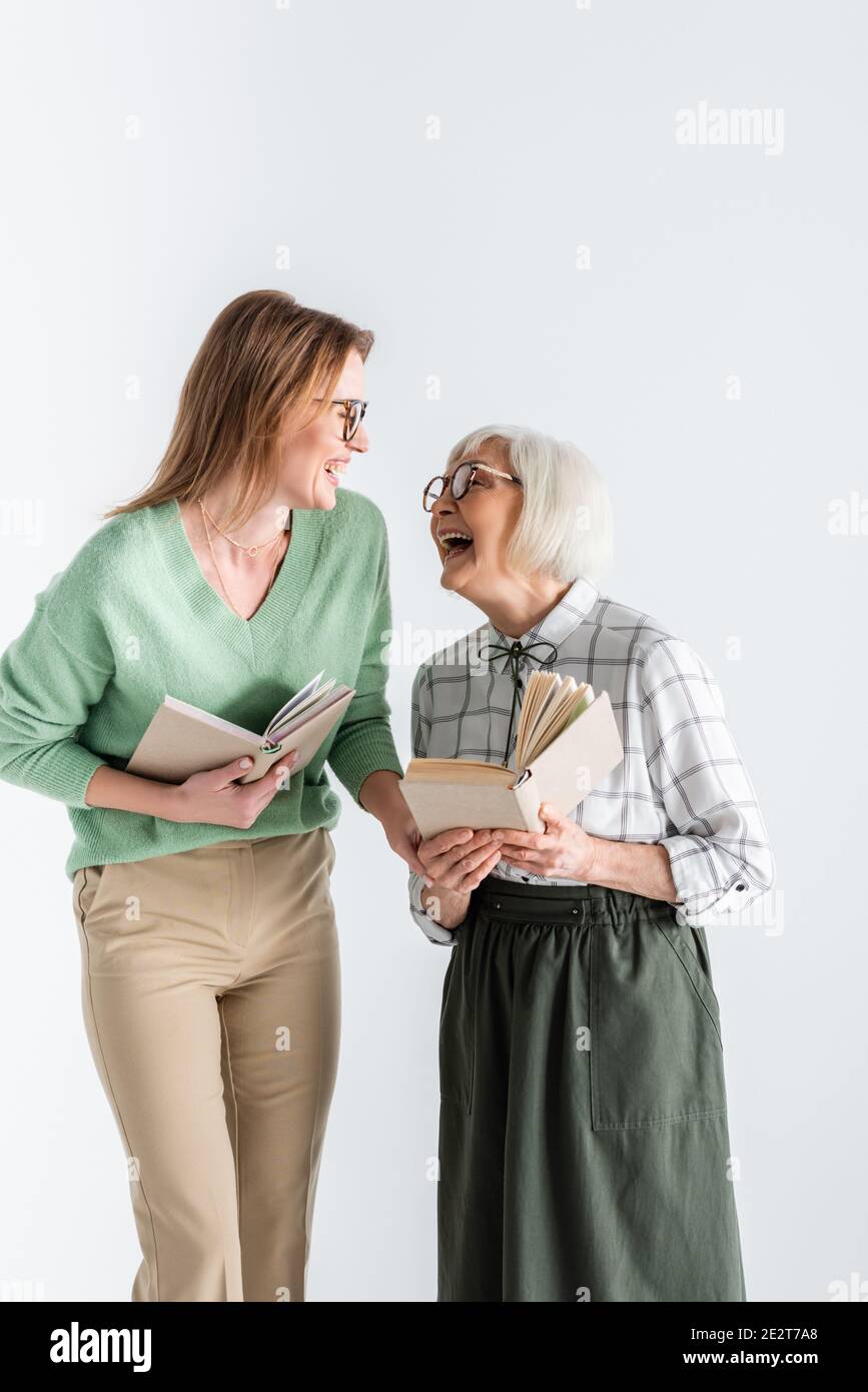 Ältere Mutter lacht mit Tochter in Brille, während sie Bücher hält Isoliert auf Weiß Stockfoto