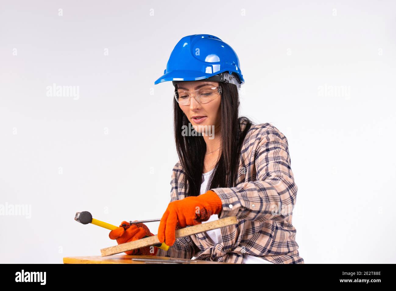 Frau in Hut mit Hammer und Nägel ist auf die Arbeit konzentriert. Weißer Hintergrund. Stockfoto