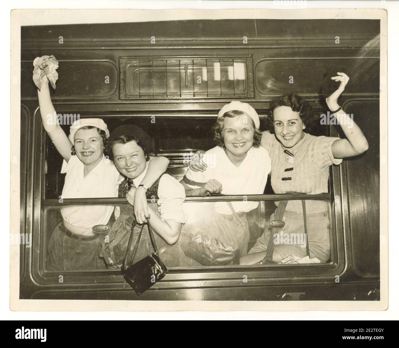 Pressefoto aus der Zeit des 2. Weltkriegs von glücklichen jungen Wanderinnen am Bahnhof, die aus einem Dampfeisenbahnfenster winken, London, Großbritannien, 1940er Jahre Stockfoto