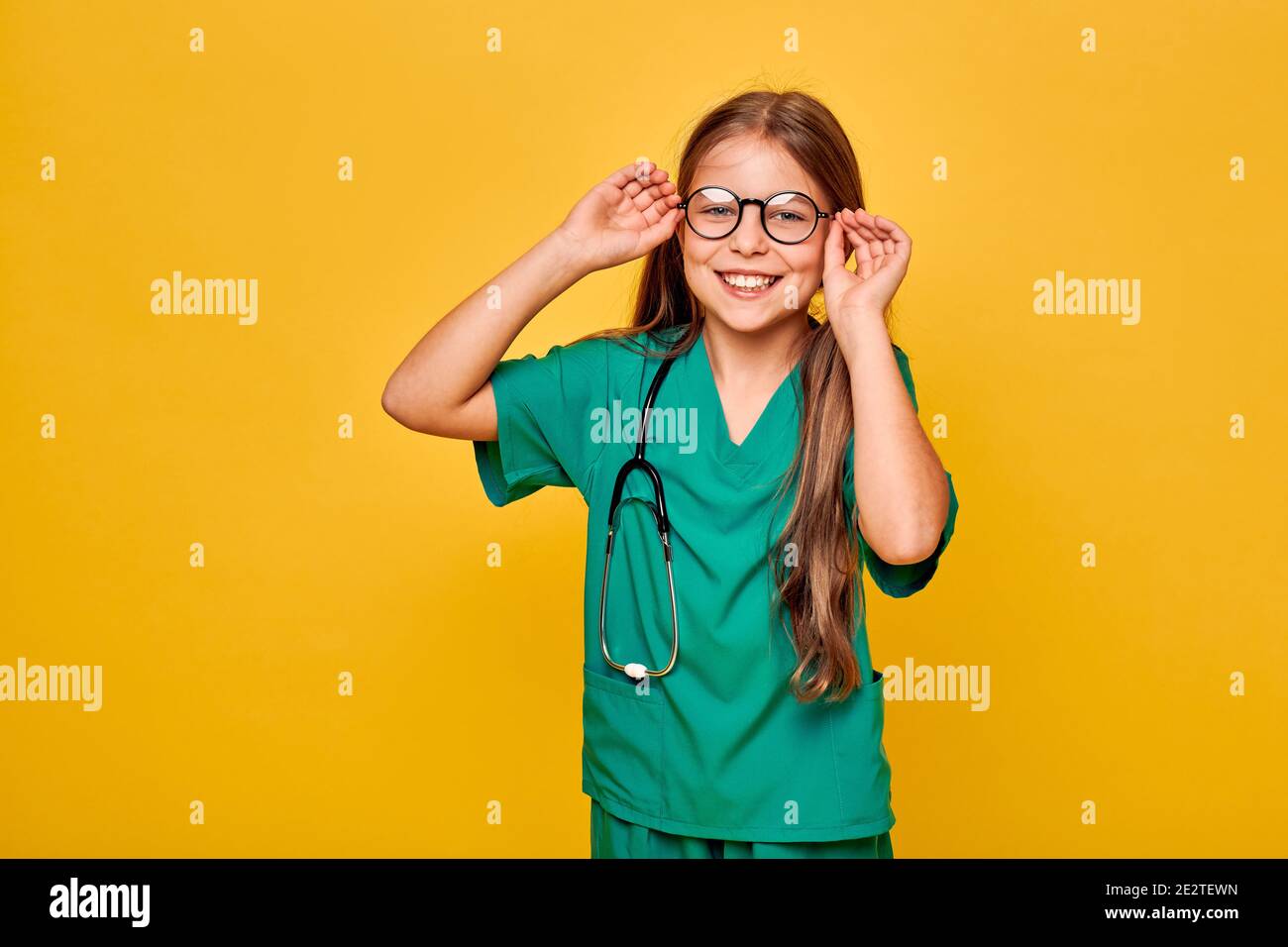 Mädchen trägt eine Brille, grüne medizinische Uniform und Stethoskop spielt einen medizinischen Beruf. Kind mit toothy Lächeln, zukünftige Arzt Stockfoto