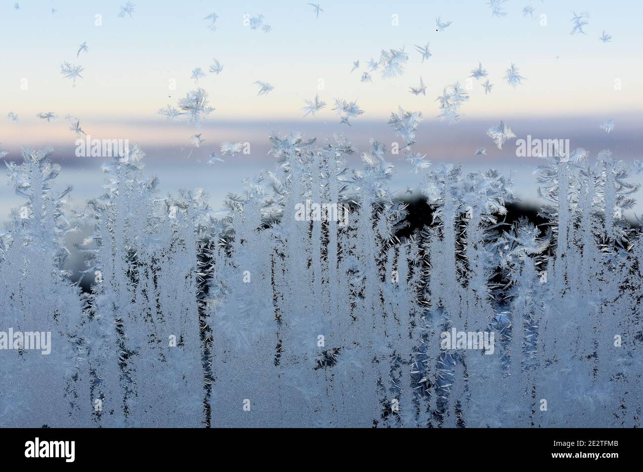 Frostmuster am Fenster mit Blick auf den Sonnenuntergang im Freien hinter Kristalle Stockfoto