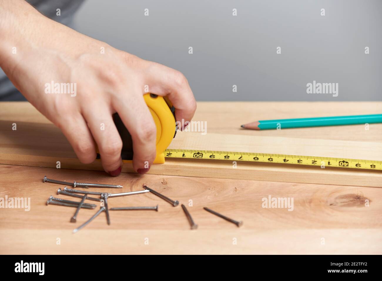 Detail einer jungen Frau, die in der Zimmerei arbeitet, mit einem Maßband, um Messungen auf einem Holzstreifen zu machen. Stockfoto