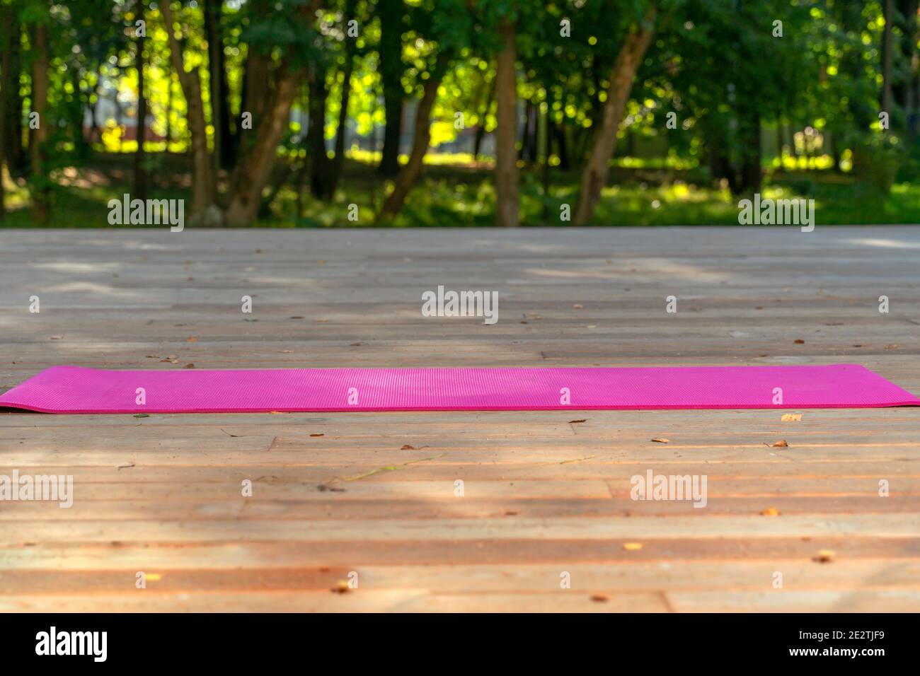 Yoga im Park. Rosa Yogamatte auf einem Holzdeck im Freien. Trainieren Sie an der frischen Luft Stockfoto