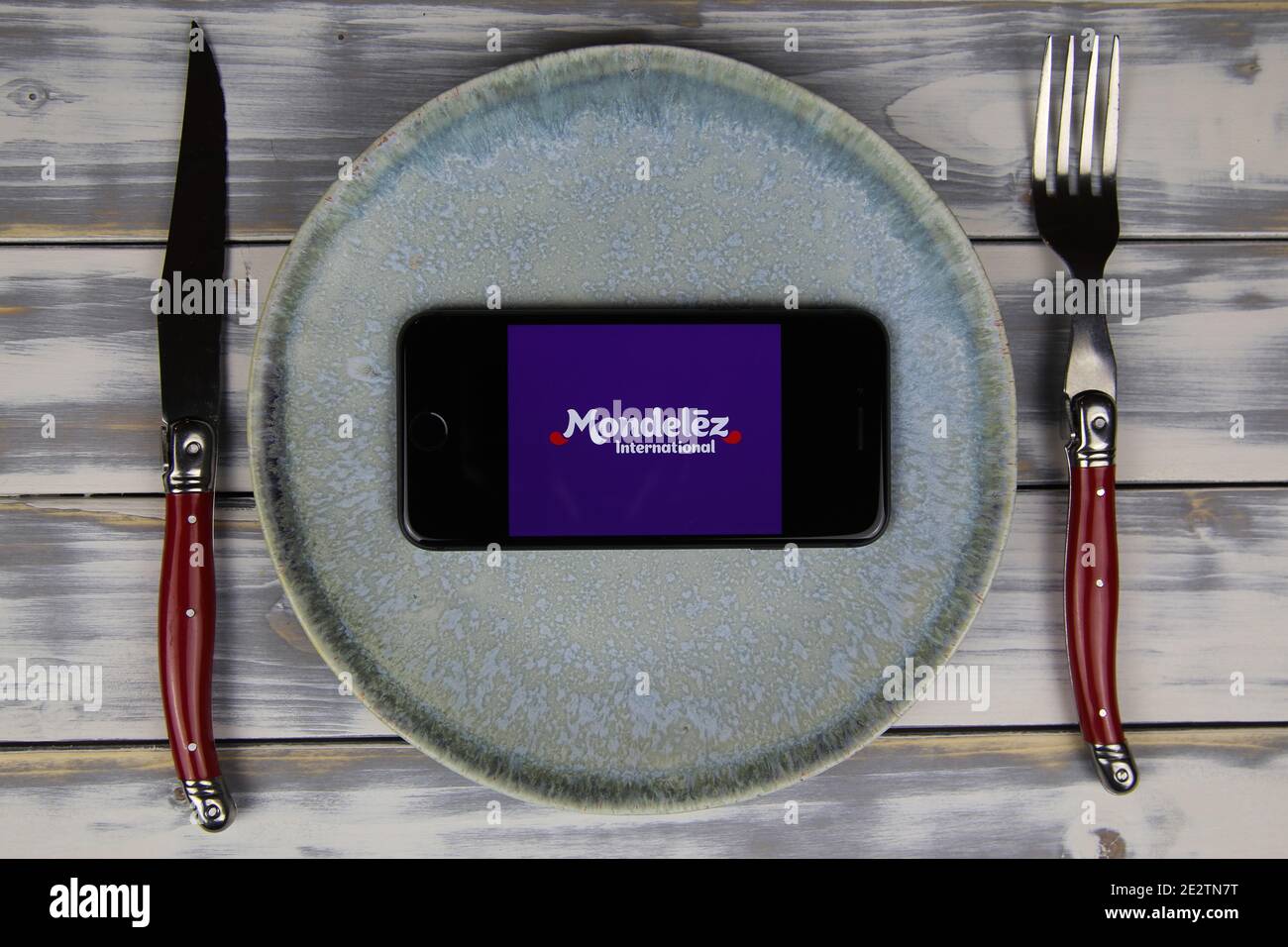 Viersen, Deutschland - 9. Mai. 2020: Nahaufnahme des Mobiltelefons auf Teller und Holztisch, Besteck mit Logo-Schriftzug der Mondelez Food Company (Schwerpunkt Mitte Stockfoto