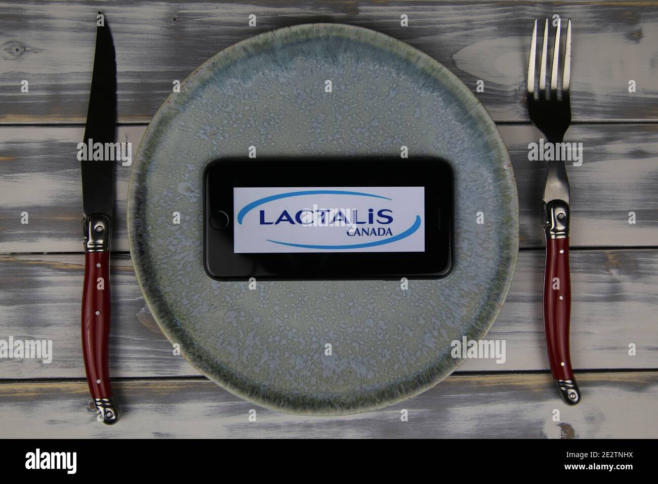 Viersen, Deutschland - 9. Mai. 2020: Nahaufnahme des Mobiltelefons auf Teller und Holztisch, Besteck mit Logo-Schriftzug der französischen lactalis Food Company (Schwerpunkt Stockfoto