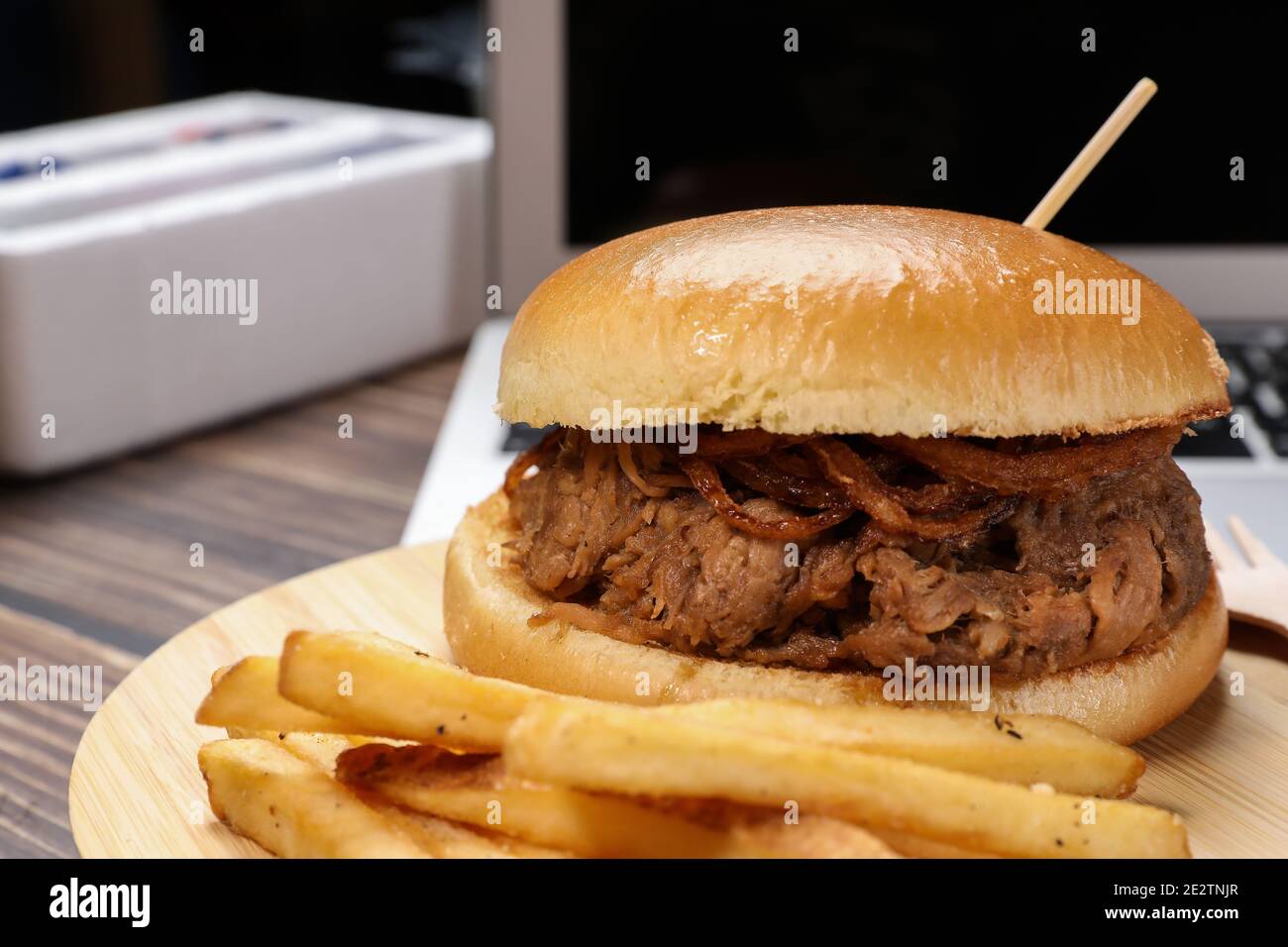 Frisch gekochter Rindfleisch-Burger mit pommes Frites vor dem Laptop vor schwarzem Hintergrund. Lieferung von Lebensmitteln zu Hause und im Büro. Stockfoto