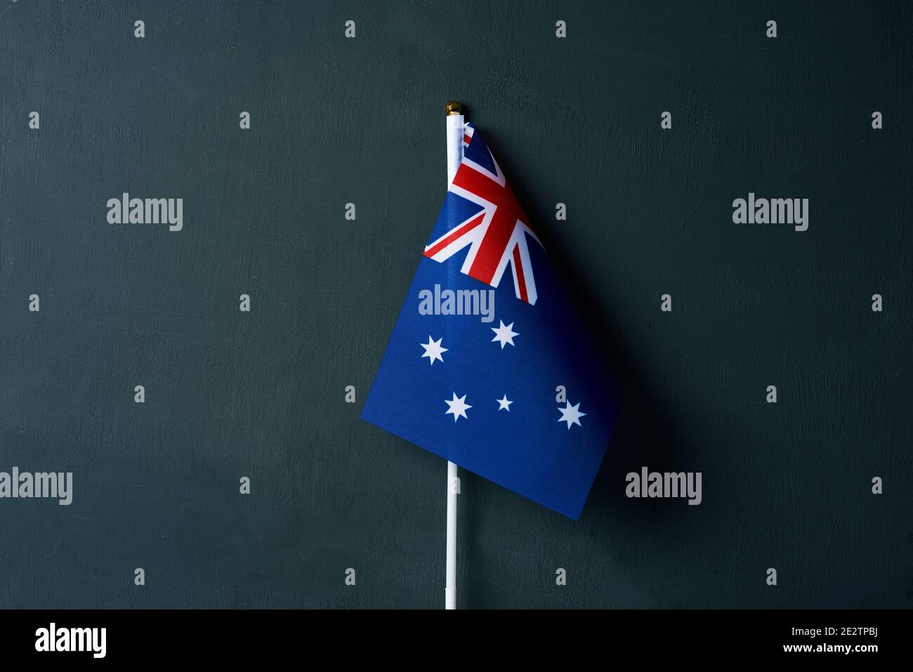 Eine kleine australische Flagge in einem weißen Pol, auf einem dunkelgrünen Hintergrund mit etwas leerem Raum um sie herum Stockfoto