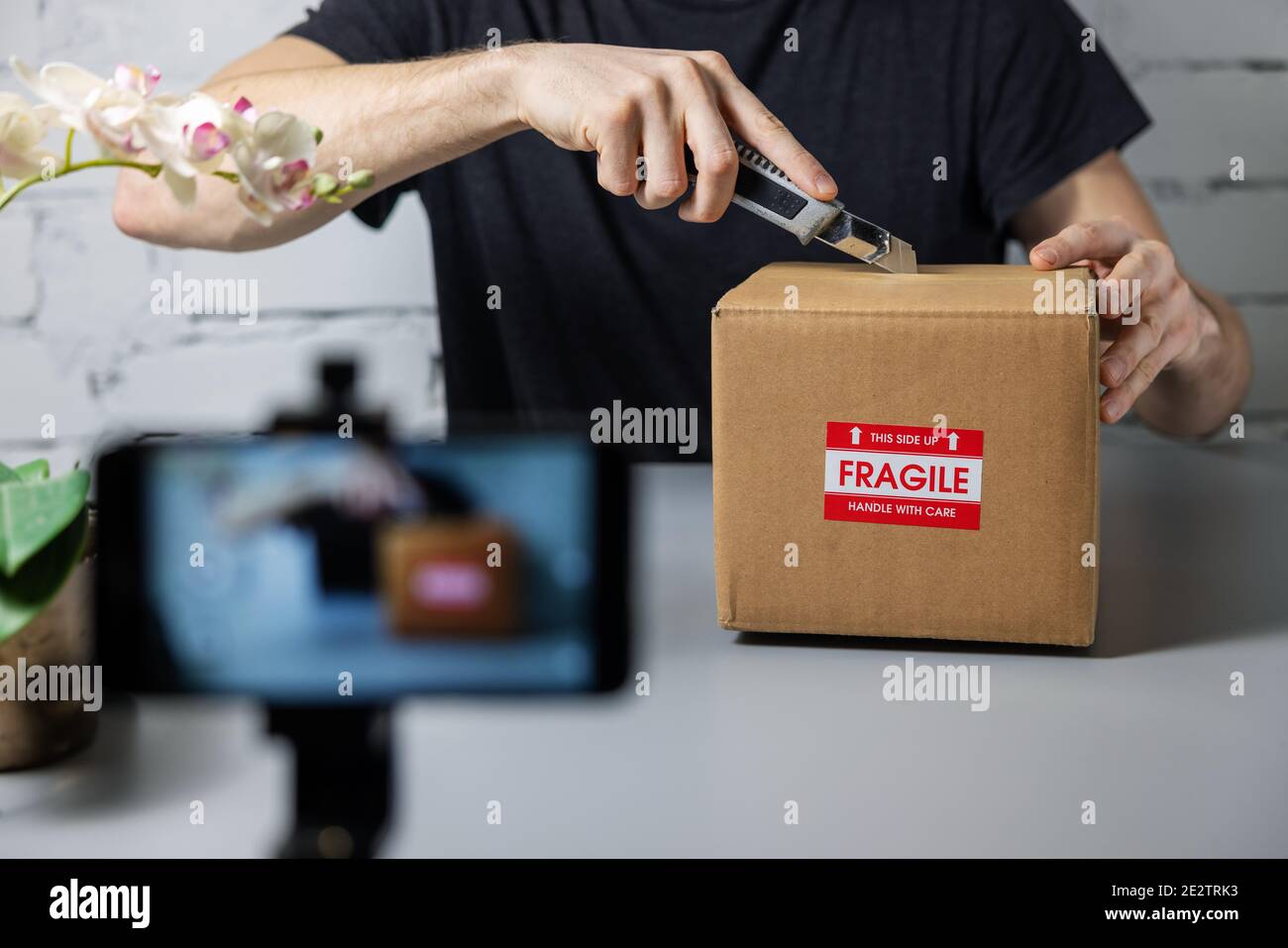 Mann Aufnahme Unboxing Video mit Handy. Schneiden Karton mit Messer. Social Media Marketing Stockfoto