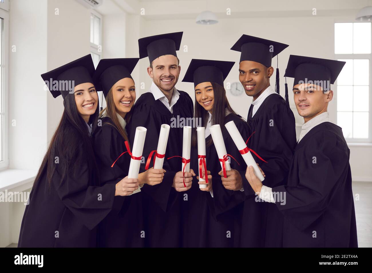 Gruppe von glücklichen multiethnischen Hochschulabsolventen in schwarzen Mantles stehend Mit Diplomen in den Händen Stockfoto