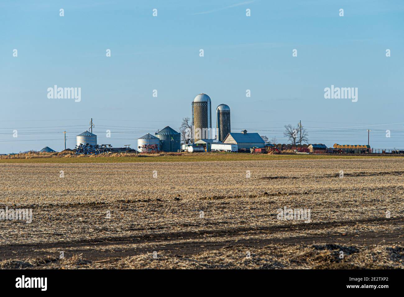 Bare Ground Winter Farm Feld mit Bauernhof Silos, Gebäude & Ausrüstung im Hintergrund. Stockfoto
