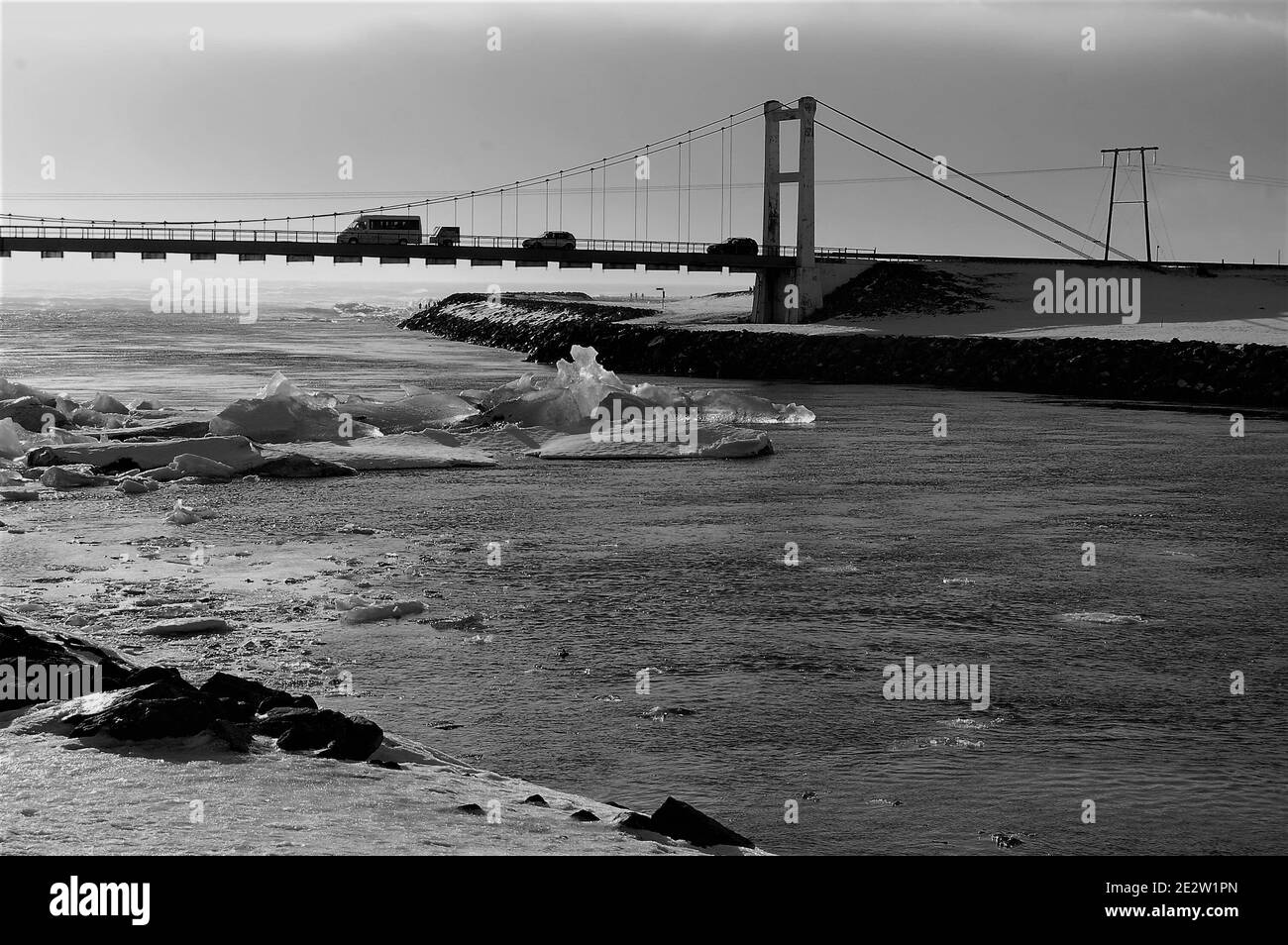 Brücke über den Fluss, der die Jökulsárlón-Gletscherlagune mit der verbindet Ozean in Island mit einigen Eisfelsen, die auf dem Wasser schwimmen Bei Winterbeleuchtung Stockfoto