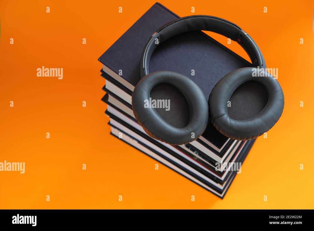 Hörbücher.Lesen. Schulung und Wissen. Fernunterricht. Ein Stapel von Büchern und Kopfhörern auf einem leuchtend orangefarbenen Hintergrund. Hörbücher, E-Books und Stockfoto